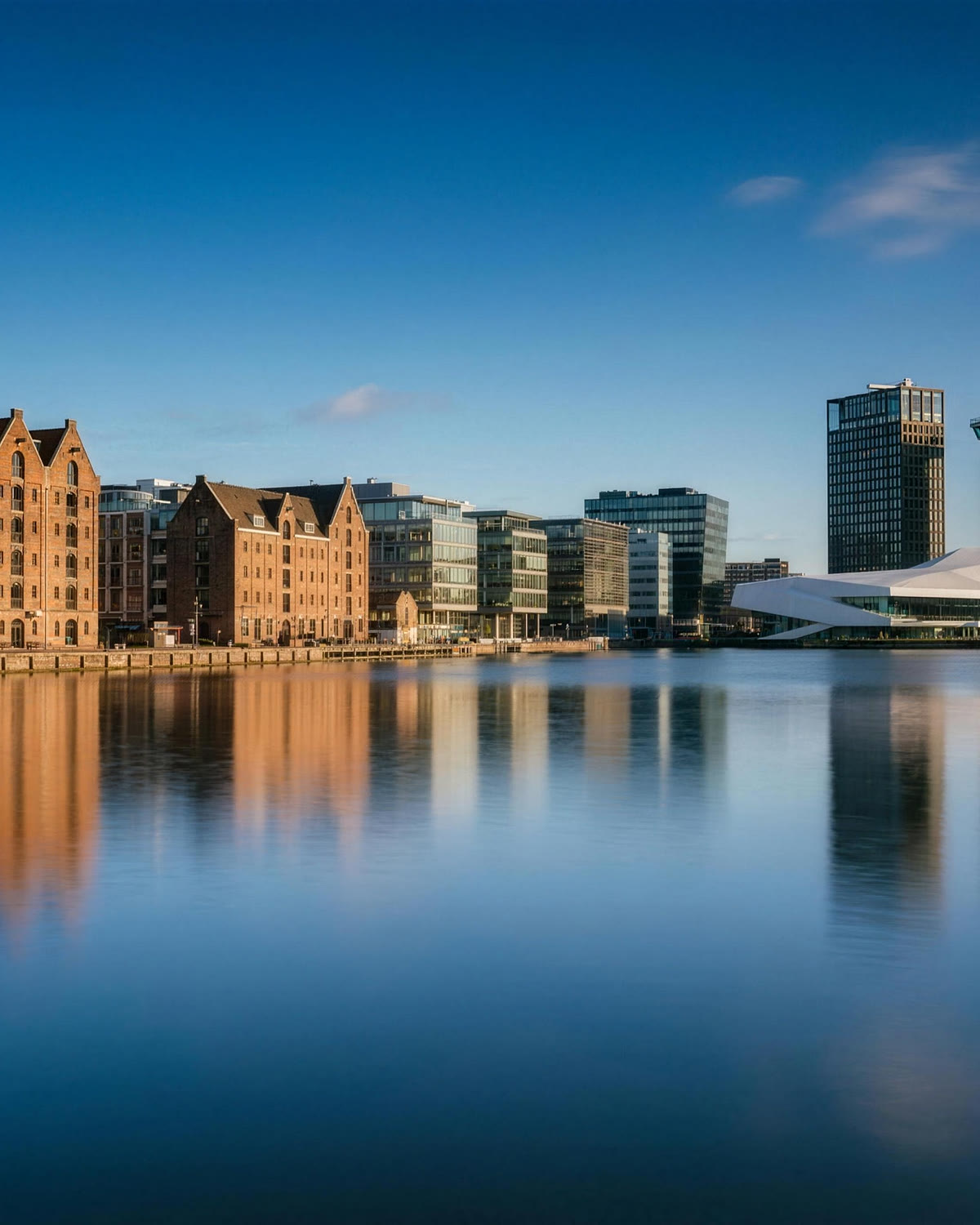Pakhuizen en moderne architectuur aan het IJ in Amsterdam op een heldere dag, weerspiegeld in kalm water